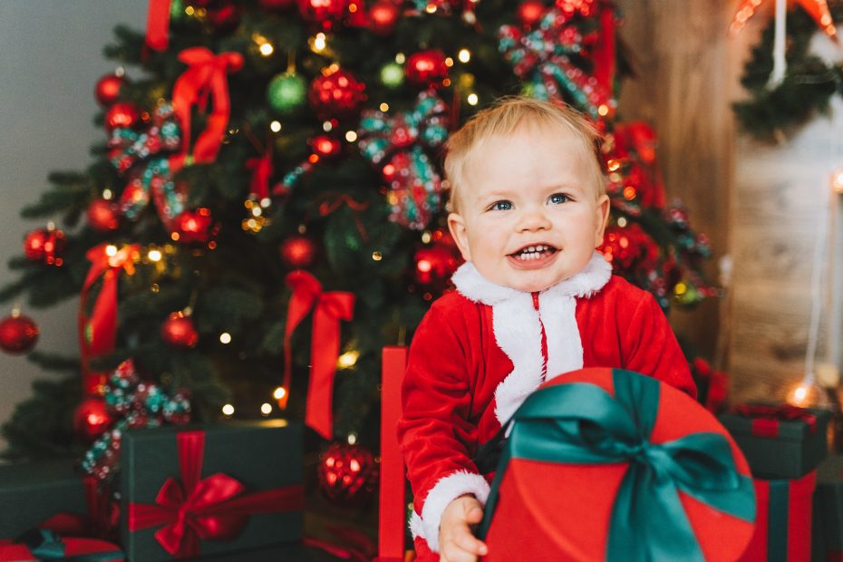 Child in Santa outfit playing by Christmas tree on Christmas Eve