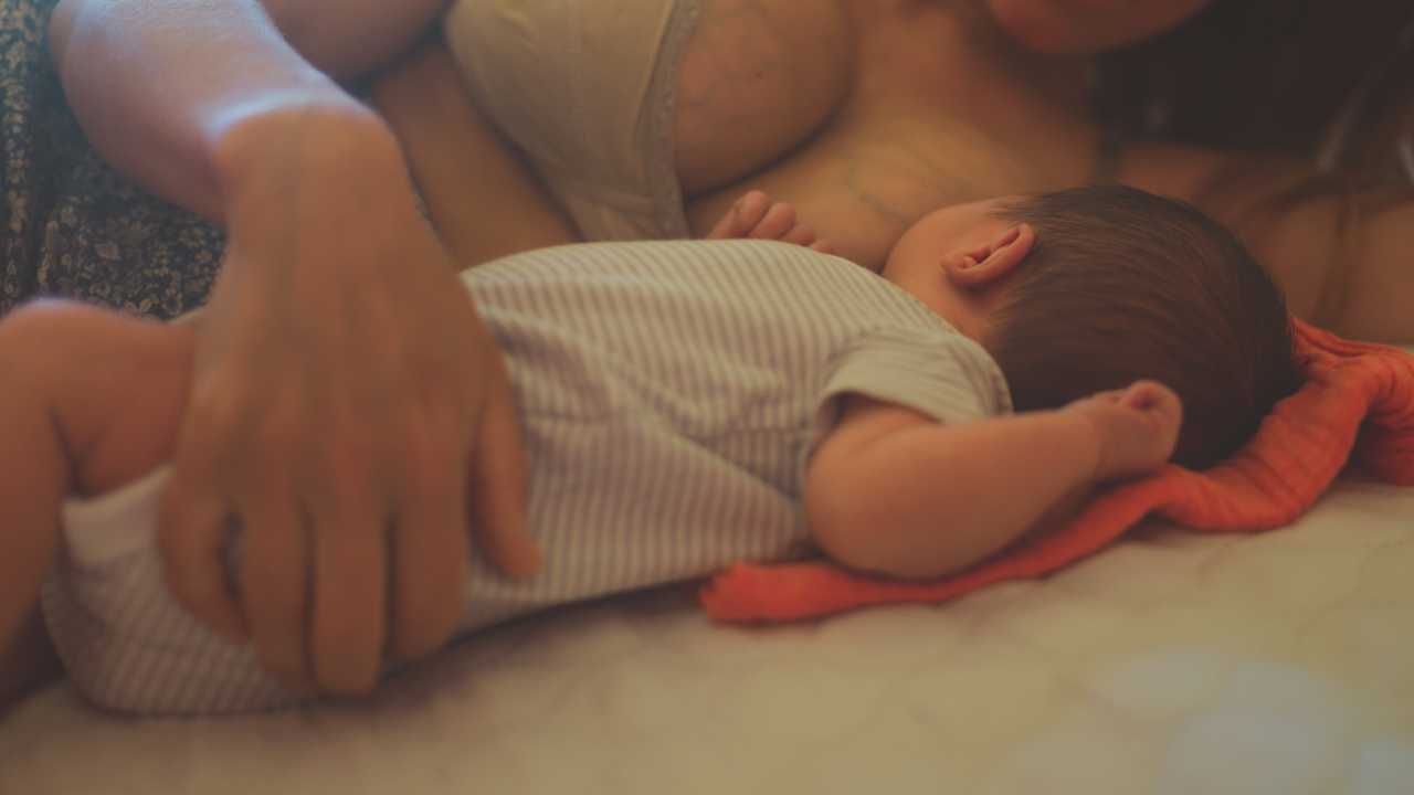 baby lying on bed with mother only sleeping latched on all night