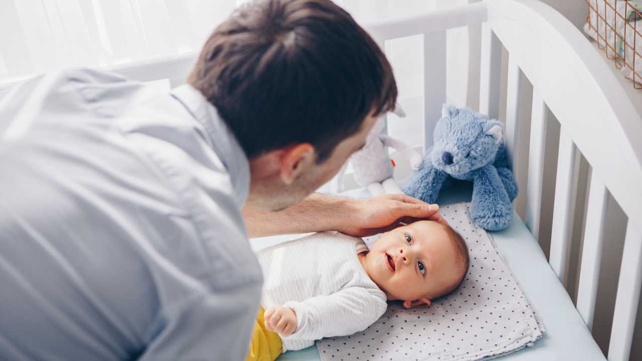 dad settling baby in cot at bedtime by stroking baby's face