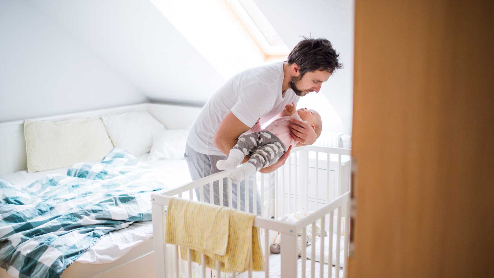 A Dad trying to transfer baby asleep into the cot as having difficulty settling at bedtime and in the night